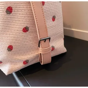 Detailed close-up of premium metal buckle and strawberry pattern on corduroy bag