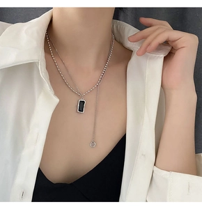 Double-layered necklace with black rectangular pendant and silver beads on a model