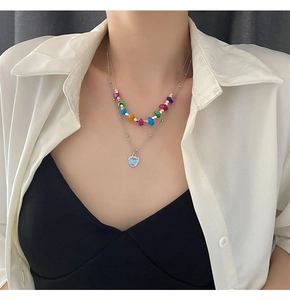 Détail d'un collier de perles colorées et chaîne argentée avec pendentif cœur violet