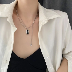 Double-layered silver necklace with black rectangular pendant and small ring charm on neck