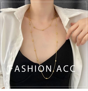Close-up of a layered gold long necklace with delicate metal beads on white shirt