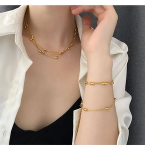 Detailed view of triple-layer gold bead necklace and double-layer bracelet on a model
