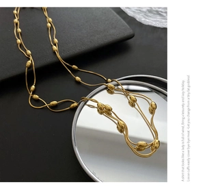 Macro detail of gold layered necklace with olive beads on black mirror surface