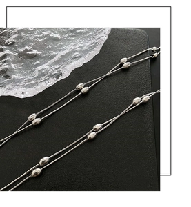 Close-up of double-layer silver titanium steel necklace with oval beads on black background