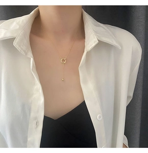Dettaglio macro della collana a Y dorata con anello intrecciato e nappa sottile pendente