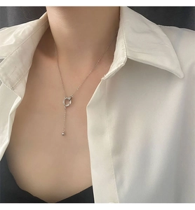 Dettaglio della collana con anelli d'argento intrecciati e nappa su camicia bianca
