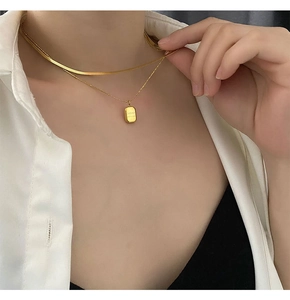 Detail of layered gold double necklace with flat snake chain and engraved rectangle pendant