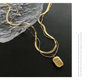 Detail of a double-layered gold snake chain necklace with an engraved rectangular charm