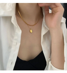 Detail of layered gold titanium necklace featuring snake chain and rectangular pendant