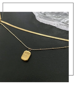 Detail view of double-layered gold necklace with flat snake chain and engraved charm