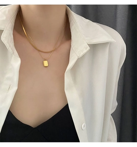 Detail of layered gold snake chain and cable necklace with engraved rectangular pendant