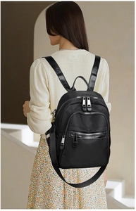 Outdoor shot of a black nylon backpack with three zipper pockets and adjustable straps