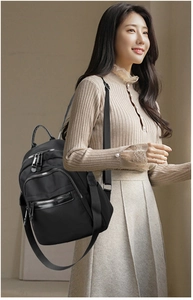 Detail of a black nylon backpack with multiple zipper pockets and wide shoulder straps