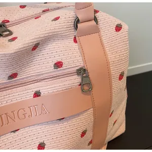 Detail of pink strawberry corduroy travel bag with metal zippers and leather handles