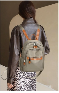 Detail view of khaki nylon backpack on model showing leather straps and zipper pullers