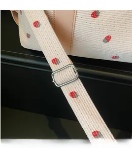 Detail of strawberry embroidery on pink corduroy fabric with silver adjustable strap buckle