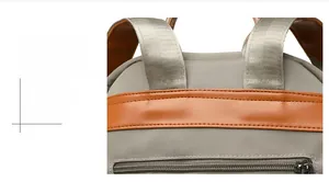 Close-up of gray canvas backpack featuring brown leather trim and reinforced stitching