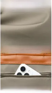 Detail of nylon backpack back zipper pocket and brown leather piping with phone for scale