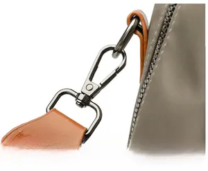 Detail of a detachable metal hook connecting a brown leather strap to a grey nylon bag