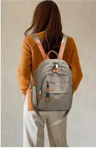 Rear view of khaki waterproof backpack with brown leather details on model's shoulder