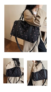 Detail view of black canvas travel bag with red strawberry print and leather handles