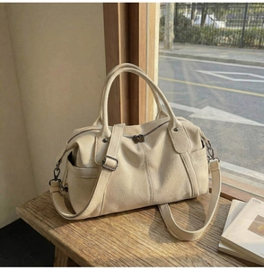 Detail of cream pebbled leather Boston bag showing side pocket and texture on wood table