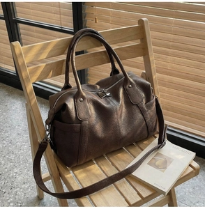 Detail of dark brown lychee leather tote bag with silver zipper on a wooden chair