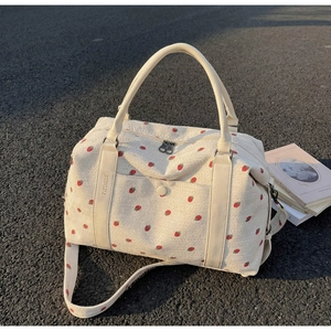 Detail of strawberry print corduroy travel bag with dual handles and golden sunset light