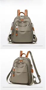 Detail view of khaki nylon backpack with multi-zipper pockets and brown leather handle