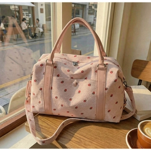 Detailed close-up of pink corduroy travel bag featuring red strawberry prints and logo
