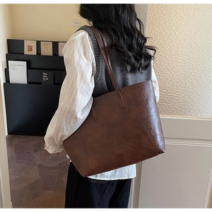 Dark brown leather tote bag with vintage texture shown on shoulder for size reference