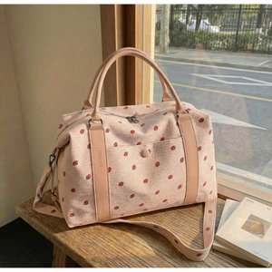 Detailed shot of pink corduroy travel bag with strawberry print on a wooden bench