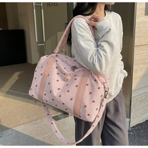 Pink corduroy travel bag with strawberry prints and adjustable shoulder strap worn by model