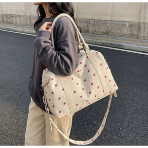 Detail of strawberry print travel bag showing textured fabric and durable leather handles