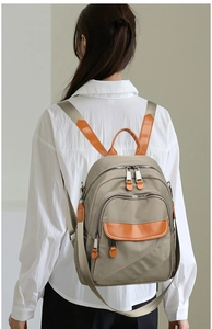 Detailed back view of khaki nylon backpack with brown leather accents on a female model