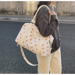Detail of cream corduroy travel bag with strawberry embroidery worn by a model outdoors