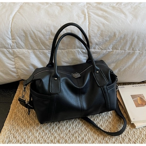 Close-up of black pebble leather Boston bag with decorative stitching and round handles