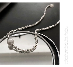 Gros plan d'un collier asymétrique avec billes d'argent irrégulières et perle centrale