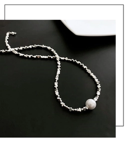 Détail d'un collier asymétrique argenté avec perle blanche sur fond noir élégant