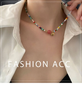 Close-up of colorful beaded necklace with a red orb and gold heart pendant on model