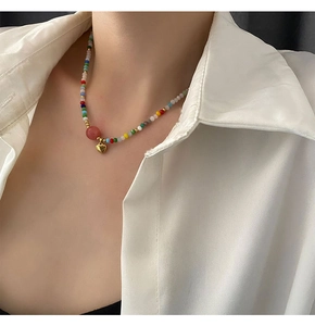 Detail of colorful beaded heart necklace with gold pendant on model wearing a white shirt
