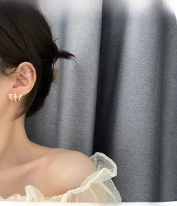Close-up of golden triple floral climber earrings with white stones on a model