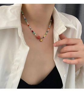 Detail of colorful beaded necklace with golden heart pendant and pink bead on neck