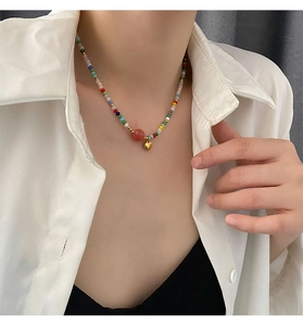 Close-up of colorful beaded necklace with large pink bead and golden heart pendant