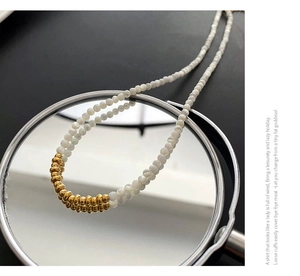 Detail of beaded necklace with white pearls and gold accents reflected on mirror surface