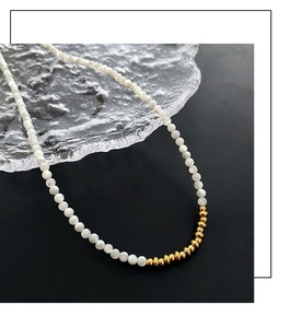Detailed close-up of white beads and gold textured metallic links on a pearl necklace