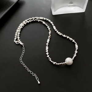 Collier de perles argentées asymétriques avec pendentif perle blanche sur fond noir