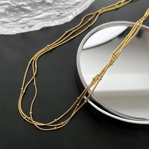 Collier multicouche doré à maille serpent avec petites billes sur fond sombre élégant