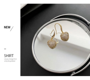 Détail macro de boucles d'oreilles cœur en or serties de zircons sur un miroir
