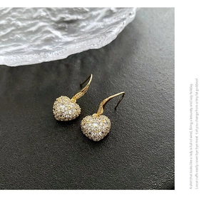 Gros plan de boucles d'oreilles cœur dorées avec cristaux micro-pave sur fond noir élégant